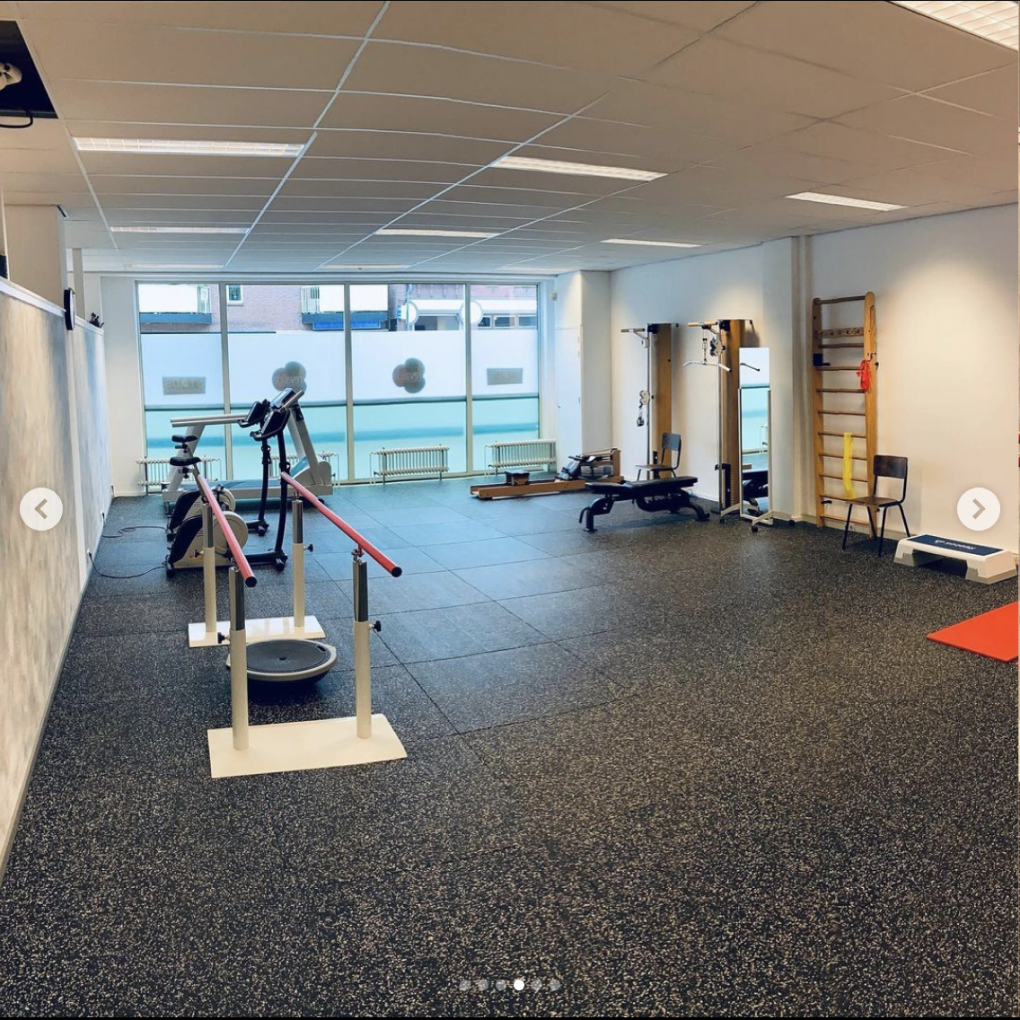 Oefenruimte met groot raam met fitnessapparatuur, wandrek en loopbrug bij STADS Fysiotherapie